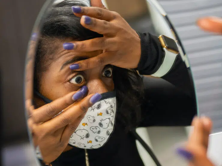 A person looks into a mirror while keeping an eye open with their hands.