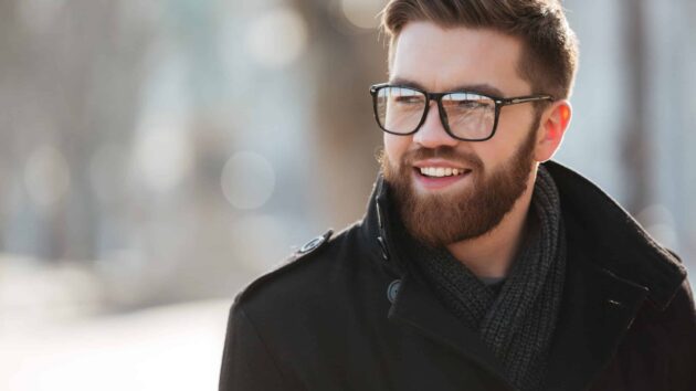 Portrait of happy bearded young man in glasses standing outdoors in winter