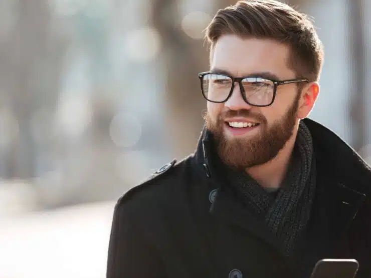 Portrait of happy bearded young man in glasses standing outdoors in winter
