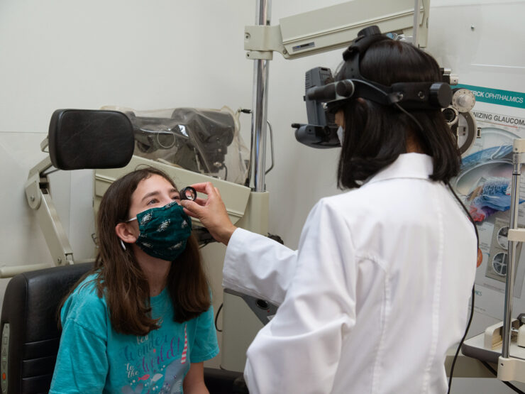 An eye doctor uses a small tool to examine a young girl's eye.