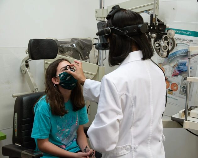 An eye doctor uses a small tool to examine a young girl's eye.