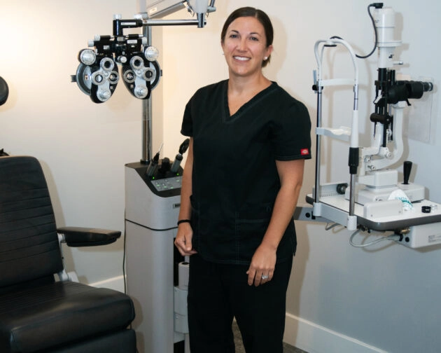 A woman in black scrubs stands in front of an eye examination machine.