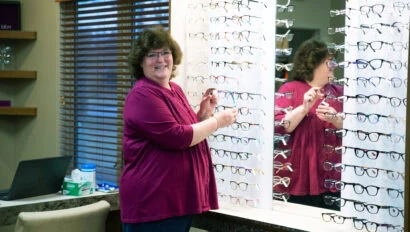 A woman in a purple shirt stands in front of a row of glasses.