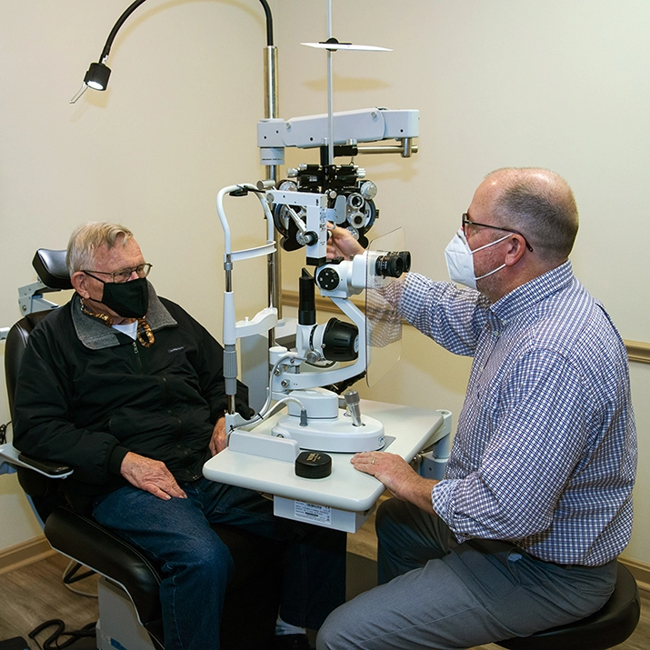 A doctor setting up eye exam equipment in front of a patient.