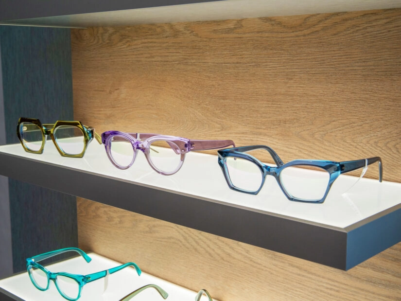 Three pairs of colorful glasses on display on a backlit shelf.