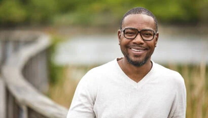 A man with black glasses looks at the camera.