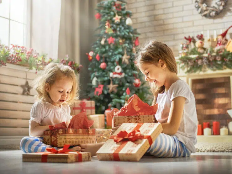 two young girls opening presents by the Christmas tree