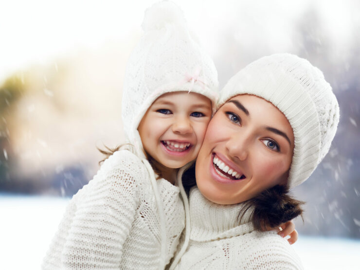 Daughter and mother wearing white knit sweaters and hats happy together