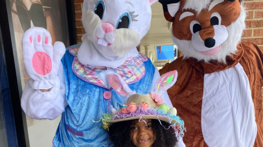 Girl in an Easter Hat standing next to the Easter bunny and a fox.