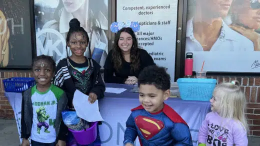 Kids smiling at a purple booth with a Simon Eye employee.