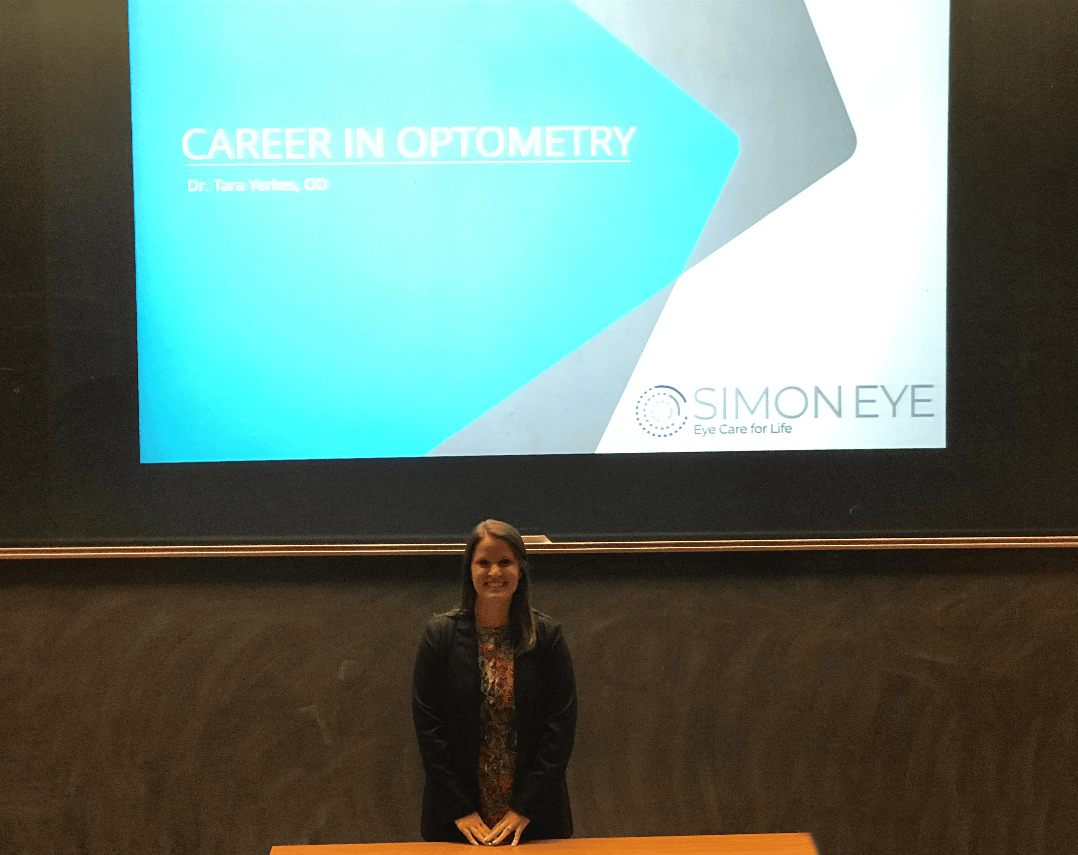 A person sits in front of a presentation slide titled "Career in Optometry" with "Simon Eye" and the tagline "Eye Care for Life" displayed on a screen behind them.