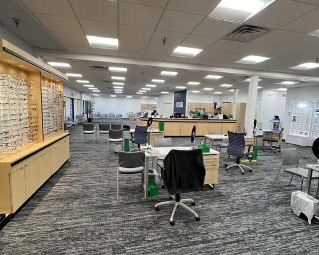 A spacious eye care clinic with multiple workstations, chairs, and a display of eyeglass frames against one wall, illuminated by overhead lighting.