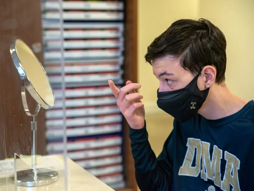 A boy puts in contact lenses in front of a mirror.