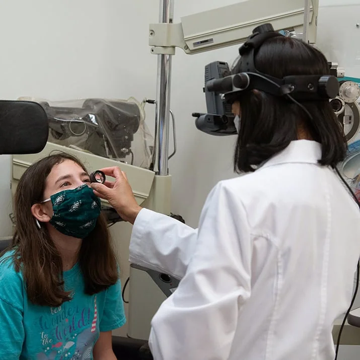 An eye doctor uses a small tool to examine a young girl's eye.