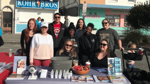 A group of people stands behind a table with various informational pamphlets and items.