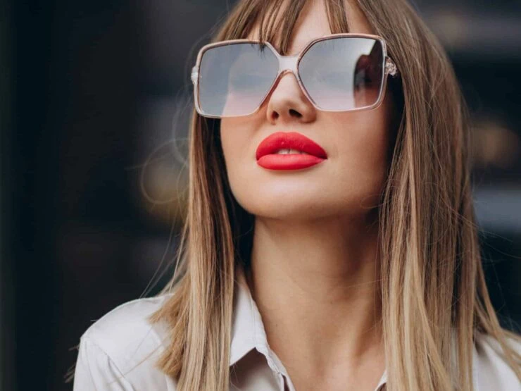 A woman with blonde hair wearing sunglasses and red lipstick looks upward.